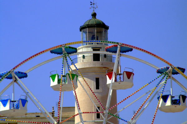 A cantilevered observation wheel with the Lighthouse of Alexandroupoli in the background.