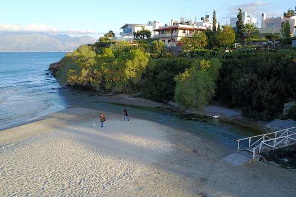 A beach separated from a tree-covered hill by a stream t Almyros Beach, Agios Nikolaos.