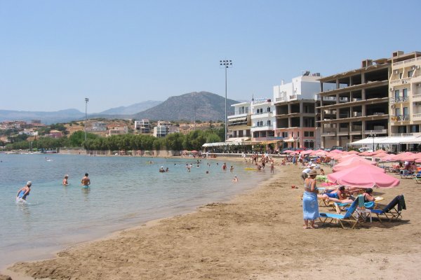 Loungers with pink umbrellas on the Agios Nikolaos (Ammos) Beach with blocks of apartments in the background.