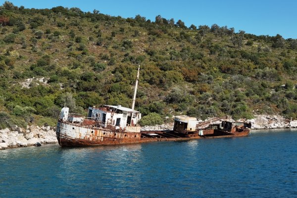 A rusty shipwreck partly submerged by the rocky coast of Peristera.