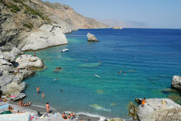 A small beach and blue waters surrounded by boulders and rocks, and Amorgos landmass in the background at Agia Anna beach.