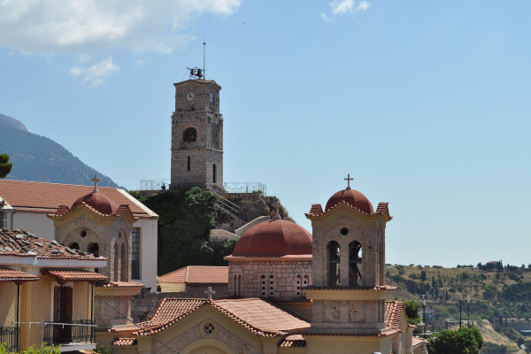 A picture showing the Clock Tower of Arachova among the houses and the church of the settlement.