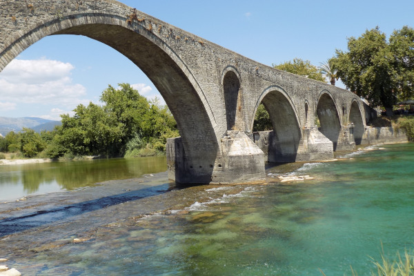 A picture of the Arta's Bridge among the green waters and the dense vegetation of the shore.