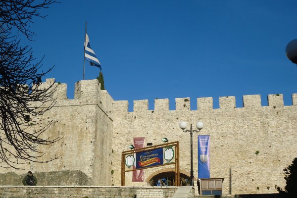 A stonewall and one of the gates of Arta's Castle under a Greek flag.