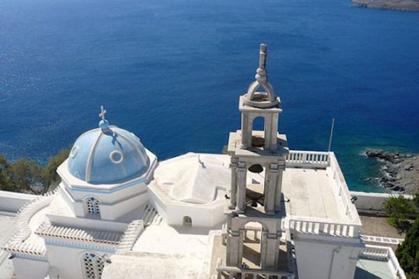 An overview of the Panagia Portaitissa Church on Astypalaia with its dome and belfry and the sea in the background.