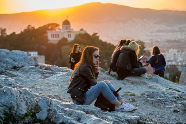 A girl smokes and friends chat at sunset on Areopagus Hill.