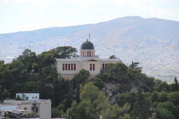 The National Observatory of Athens is a crème-color neoclassic building with a dome inside the woods.