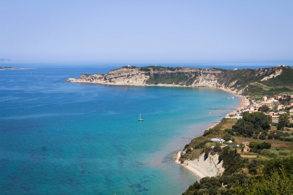 A bay with a settlement and a beach, and a sailing boat in the blue, Agios Stefanos Beach, Avliotes.