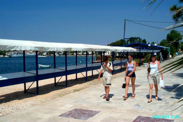 A picture of three persons walking by stands on the paved seafront promenade of Eretria.