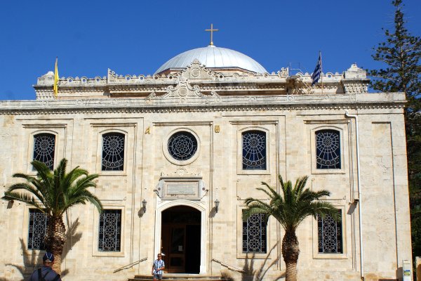 Agios Titos is a rectangular building with a dome, decorated windows, and two palm trees at the entrance.