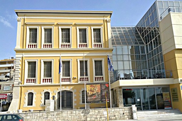 A yellow neoclassical building and a modern glass and steel building at the Historical Museum of Crete.