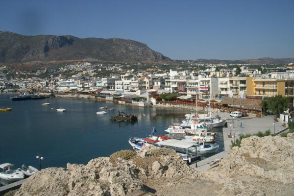 An overview of the Hersonissos Port that includes some boats anchored by the coast and a part of the settlement.