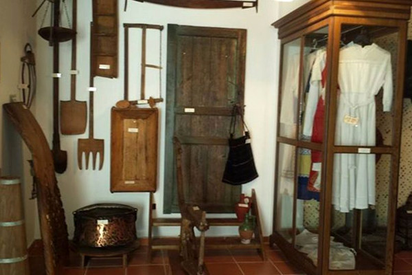 A room of the Polichrono Folklore Museum with traditional garments in a display and other exhibits hanging on the walls.