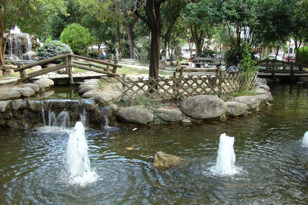 A fountain in the lake, paths, and a small stream within the green environment of the Katerini Municipal Park.
