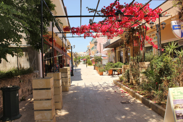 A photo showing a pedestrian street with flowers overhanging in Lixouri.