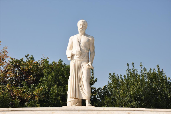 The statue of Hippocrates in Larissa made of white marble with trees in the background.