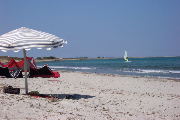 A picture with an umbrella and a windsurfer in the background taken on the beach of Keros on Lemnos island.