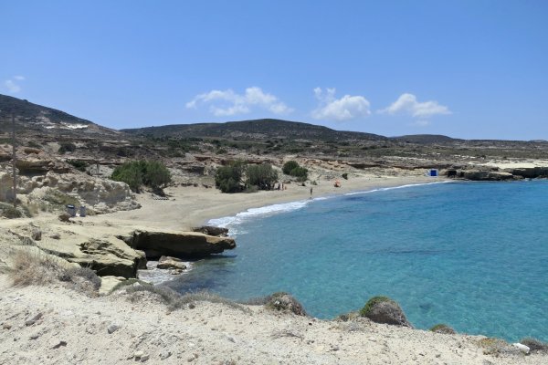 A sandy beach with a rock on one side and low-vegetation hills in the background at Alogomandra, Melos.