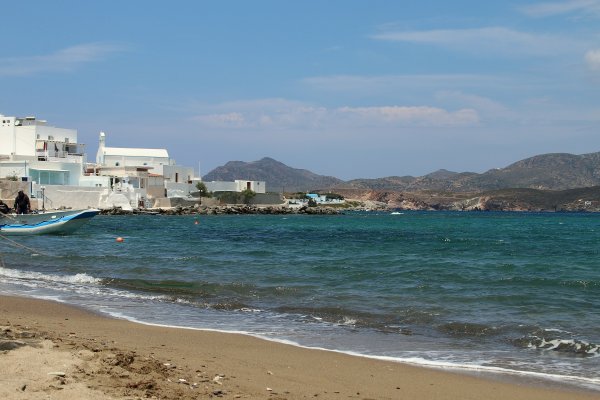 A few white buildings on the left and in the background the island of Kimolos, view from Pollonia beach.