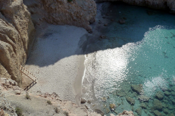 Crystal-clear waters at Tsigrado Beach of Milos between cliffs, and the wooden ladder, the last step of the trip there.