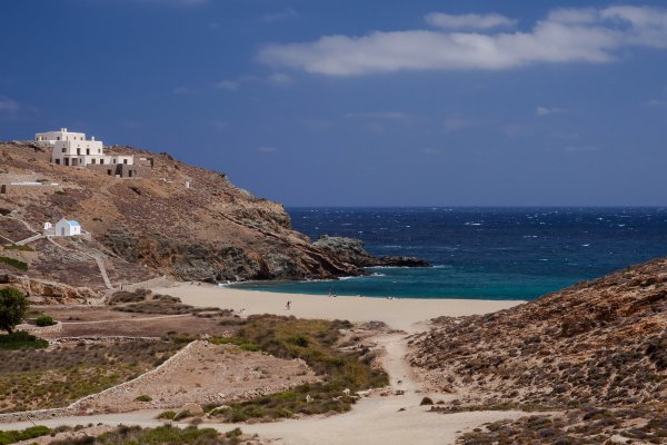 The deep blue sea in the background is succeeded by turquoise waters, and the desert-brown sand of the Fokos Beach, Mykonos.