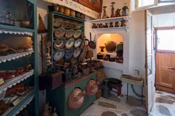 A white wall with shelves full of plates, bottles, and pottery at the Kastro House Folk Museum.