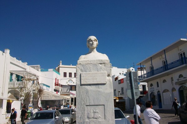 Bust of Mavrogenous against the blue sky with low white buildings in the background.