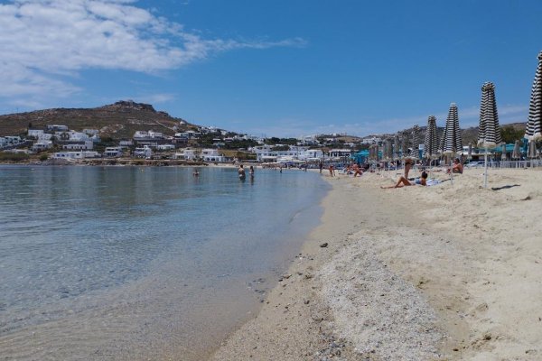 A photo of Ornos Beach and it's crystal clear waters. In the background the newly built right side of the settlement.