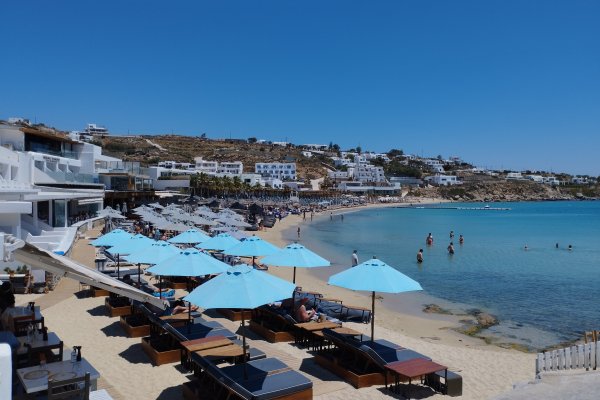 Turquoise waters, lines of straw beach umbrellas, and a series of white houses at Platis Gialos Beach, Mykonos.