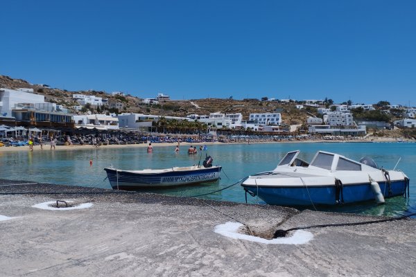 Two boats are anchored in a small pier. In the background a view of the Platis Gialos settlement and its beach.