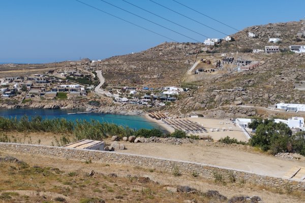 Super Paradise bay in Mykonos between two arid-brown hills with a sporadic houses.