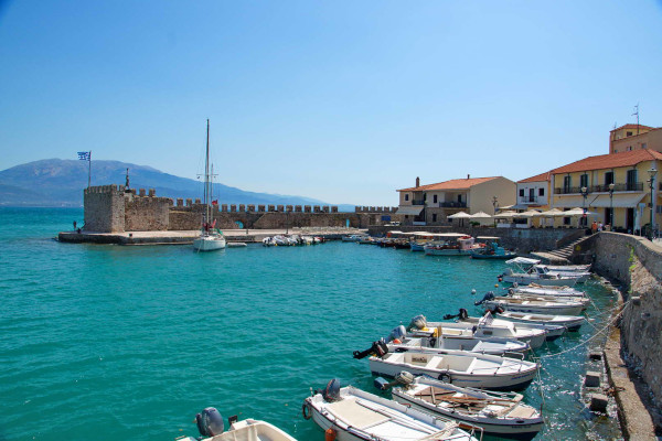 A photo showing the fortified port of Nafpaktos with many small boats anchored by the coast.