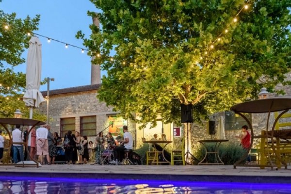 An old stone building elegantly lit, tables an chairs, and people enjoying drinks standing at FOUGARO Art Center.