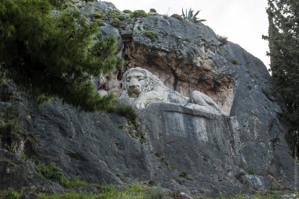 A white Lion of Bavaria carved in a grey boulder. The lion is in resting position and has a sad facial expression.