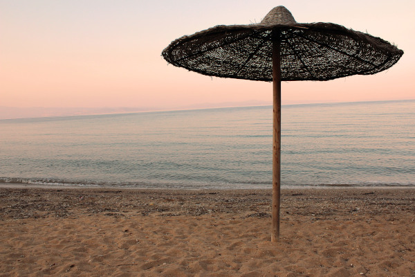 A straw-woven sun umbrella and the calm sea in the background during the evening before dusk.