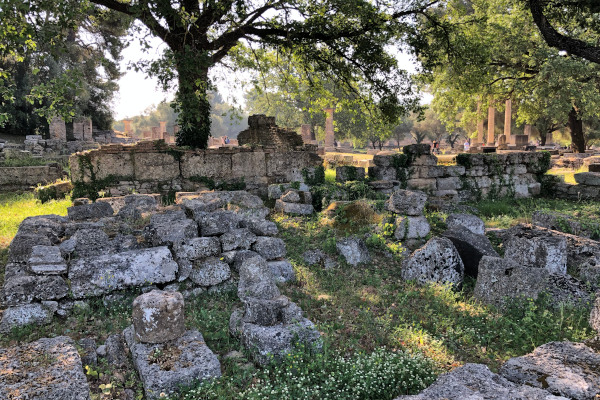 A picture of the remains of the Prytaneion of Olympia on grass below trees.