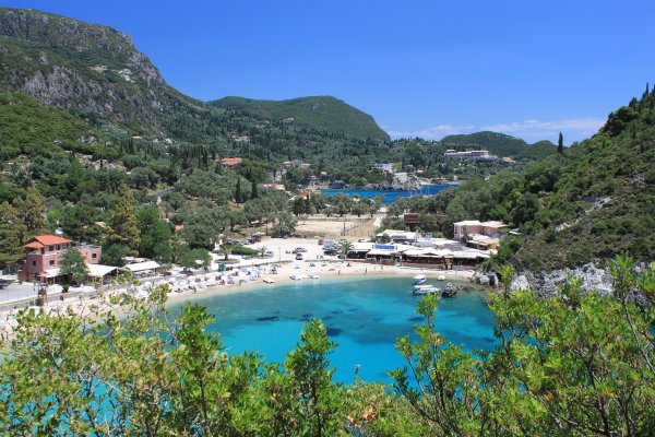 Agios Spiridon or Paleokastritsa beach with turquoise waters surrounded by green, rocky hills.