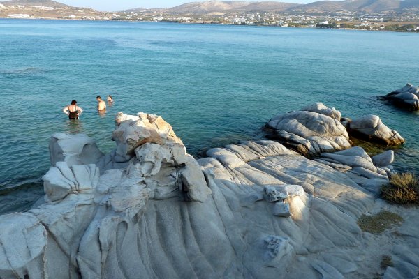 Rocks with a smooth surface sculpted by the waves, and a few people in the sea at Kolymbithres Beach, Naousa, Paros.