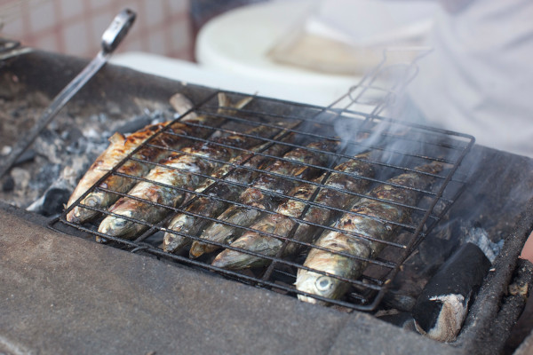 A picture showing six sardines on a grill and a grill fork laying aside.