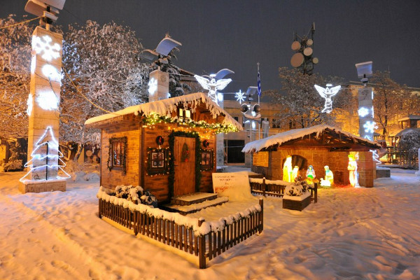 A lit up Christmas manger and other decorations in the snowy center of Ptolemaida.