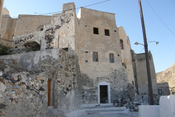 Old two-story buildings of light brown color with decaying paint and exposed rocks 