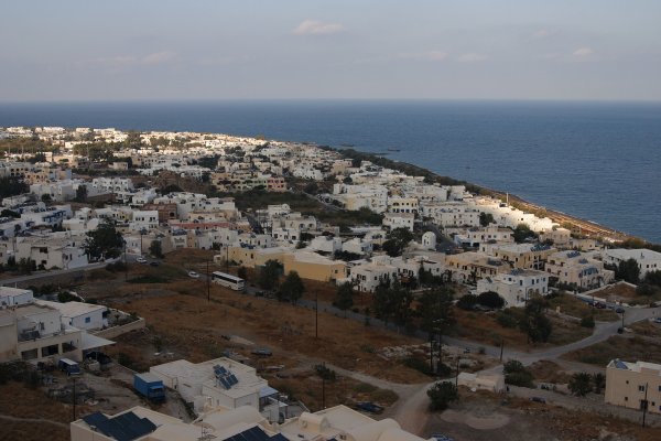A brown-soil hill taken over by white houses and the blue sea in the background.