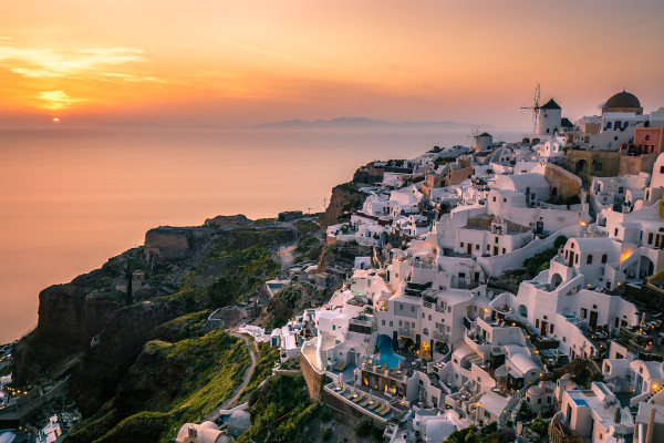 The famous sunset of Santorini and the white houses of Oia over a steep cliff.