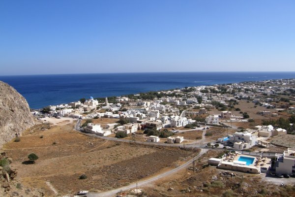 A brown-soil landscape with many white houses and a deep-blue sea in the background.