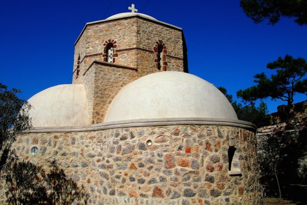 A stone-built chapel with two white domes among trees in a picture where earthy colours dominate.