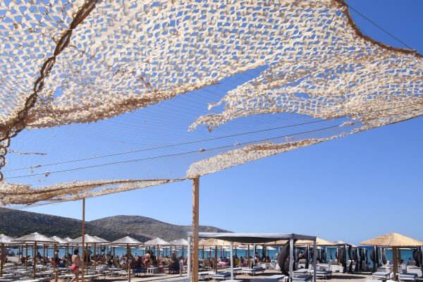 A beach bar on Anavyssos beach with dozens of umbrellas and sunbeds under a blue sky.