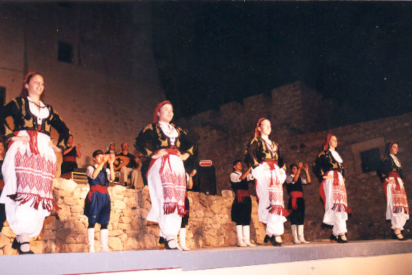 A band and dancers with traditional clothes are dancing during a performance of Kornaria Summer Festival of Sitia.