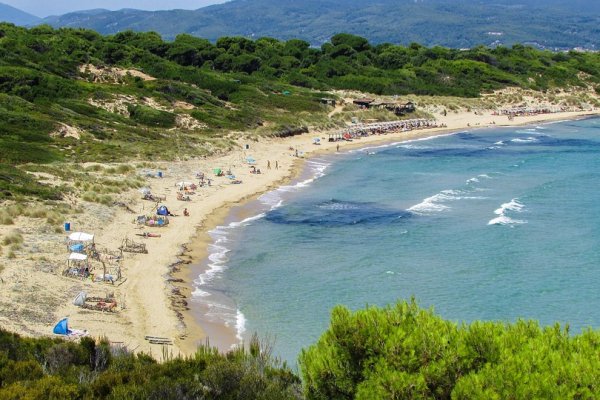 Elia Beach sandwiched between a green rise and azure sea, and people sunbathing.