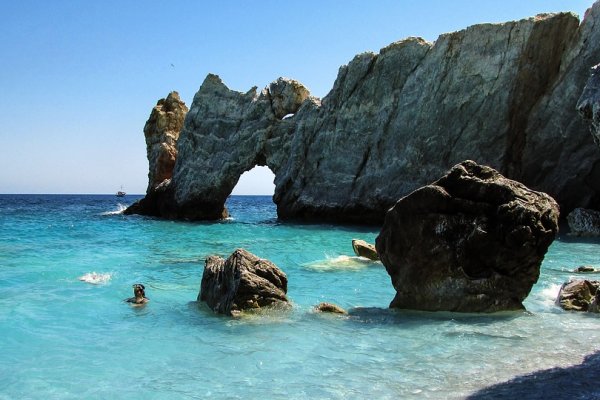 The sea arch of Lalaria beach behind scattered boulders and rocks in the turquoise sea.