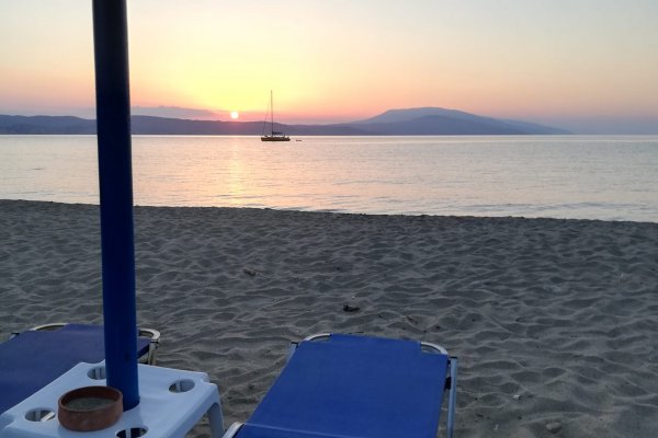 A pink-orange sunset and a sailing boat in the horizon as seen from Ligaries Beach, Skiathos.